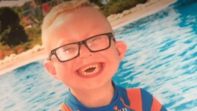 Na foto está o menino Logan Jones, em frente a uma piscina, usando óculos e com um lindo sorriso no rosto.